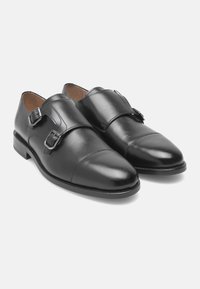 Chaussures habillées en cuir noir avec double boucle, bout rond, texture lisse et couture contrastante. Dotées d'un talon bas empilé.