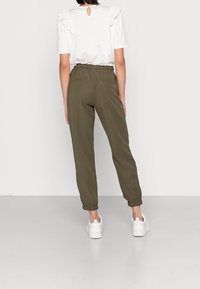 Joggers à taille élastique couleur vert olive avec des bords aux chevilles, associés à un t-shirt blanc avec détails en dentelle et une ouverture dos en forme de goutte.