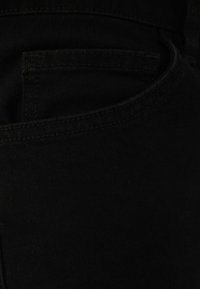 Černá denimová tkanina s hladkým povrchem, obsahující zadní kapsu s viditelným švem a klasickým designem.