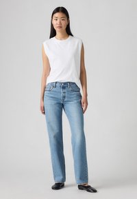 Camisa sin mangas blanca combinada con jeans rectos de denim azul claro. Los jeans presentan un suave desvanecimiento y un clásico diseño de cinco bolsillos. Bailarinas negras.
