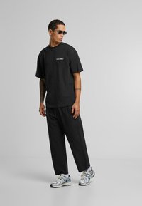 Sort bomulds t-shirt med korte ærmer, der har et lille logo på brystet. Sammen med løse sorte bukser og reflekterende sneakers.