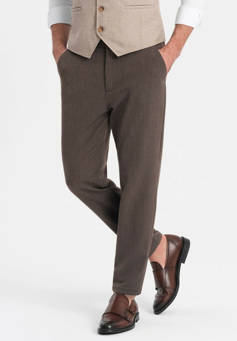 Pantalones marrones con textura y forma recta, combinados con zapatos de cuero marrón oscuro con un diseño de doble hebilla.