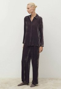 Conjunto de pijama de terciopelo en morado oscuro, que incluye una camisa de botones con cuello y pantalones de pierna ancha. Textura suave con un sutil brillo.