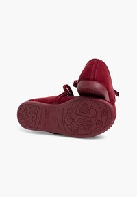 Czerwone zamszowe buty na płaskim obcasie z okrągłym noskiem, regulowanym paskiem i teksturowaną gumową podeszwą z kwiatowymi i sercowymi wzorami.