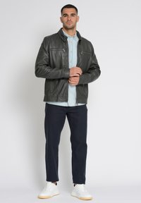 Donkergroene leren jas met ritszakken, gedragen over een lichtblauw shirt. Gecombineerd met donkere broek en witte sneakers.