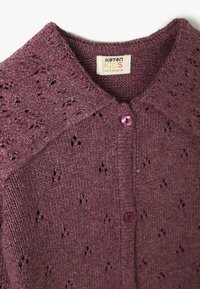 Fioletowy sweter kardigan z teksturowanym wzorem i delikatnymi detalami w formie ażurowych wstawek. Posiada okrągły kołnierz oraz pojedyncze zapięcie na fioletowy guzik.