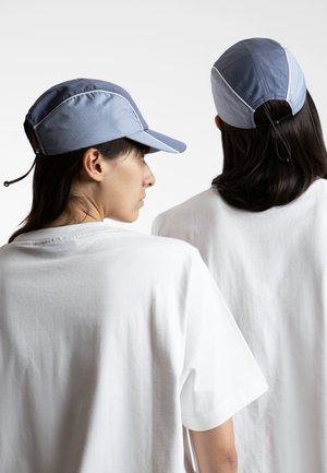 Blue cap with a curved brim and adjustable back, paired with white t-shirts. The cap features contrasting stitching and a sleek design.