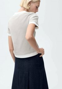 Top gri cu mânecă scurtă și guler alb, asortat cu o fustă din denim închis, cu pliseuri. Materialul pare moale și lejer.