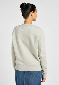 Sudadera gris claro con cuello redondo, puños y cintura acanalados; presenta una textura suave y lisa y mangas raglán.