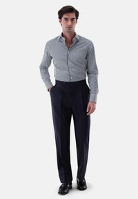 Gestreifte Hemd-Bluse in Marineblau und Weiß, kombiniert mit marineblauen, gefalteten Hosen. Schwarze Schuhe runden den smart-casual Look ab.