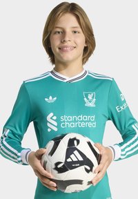Žalia vartininko marškiniai su baltais akcentais, su logotipais. Laiko juodai baltą futbolo kamuolį su Adidas prekės ženklo logotipu.
