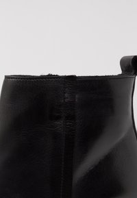 Stivale alla caviglia in pelle nera con finitura liscia, caratterizzato da una cucitura centrale e un anello sul retro per una facile calzata.