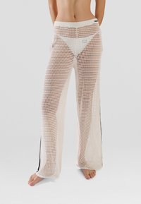 White mesh trousers with a loose fit, featuring a wide waistband and vertical black stripes along the sides. Rounded hem.