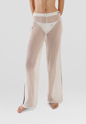 White mesh trousers with a loose fit, featuring a wide waistband and vertical black stripes along the sides. Rounded hem.