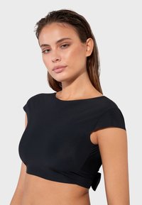 Crni kratki top s kratkim rukavima, napravljen od glatkog materijala, s prilagođenim dizajnom i malom mašnom na leđima.