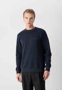Mörk marinblå tröja med rund halsringning, tillverkad av mjukt material, med en liten broderad logotyp på bröstet samt ribbade mudd och nederkant.