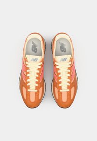 Baskets orange et rose avec un dessus en daim et en mesh, comportant des lacets crème, un bout arrondi et une semelle en caoutchouc noire.