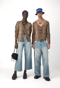Twee modellen dragen dierenprint cardigans. De linker cardigan is lichtbruin met zwarte vlekken; de rechter heeft een V-hals. Beide dragen wijde jeans en klompen.