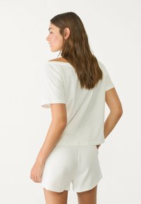 T-shirt en coton blanc avec une coupe décontractée, des manches courtes et des coutures d'épaule légèrement tombantes, accompagné de shorts blancs assortis.