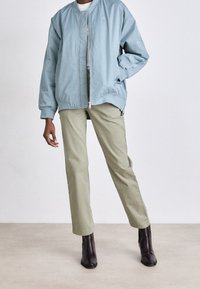 Světle modrá bunda bomber s elastickými manžetami, kombinovaná s olivově zelenými kalhotami a černými kotníkovými botami, na neutrálním pozadí.