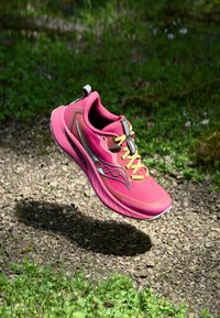 Zapatilla deportiva rosa con parte superior de malla, acentos grises en contraste y cordones amarillos. Presenta una puntera redondeada y una suela acolchada para mayor comodidad.