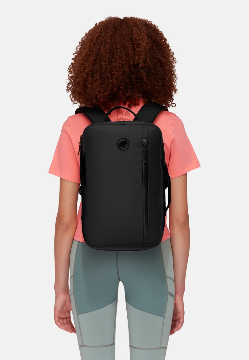 Zaino nero con una texture liscia, forma rettangolare, tasca frontale con zip e un logo circolare. Indossato con spallacci regolabili e imbottiti.