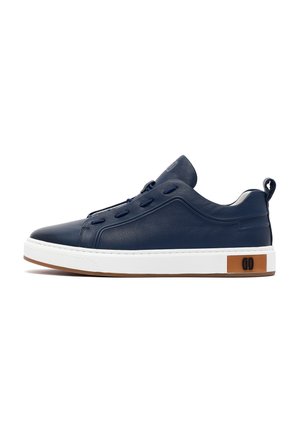 Navyblauwe lage leren sneaker met witte zool, bruin accent bij de hiel, vetergaatjes zonder veters en een trekkoord bij de hiel.
