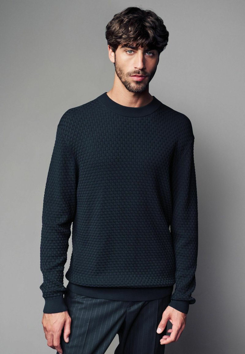 Dunkles Sweatshirt mit einer Wabenstruktur, Rundhalsausschnitt und gerippten Bündchen; kombiniert mit gestreiften Hosen.