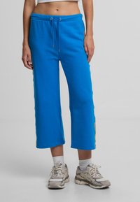 Modré zkrácené tepláky vyrobené z měkké látky, s páskem na stažení v pase a pruhovanými akcenty po stranách. Texturovaný a pohodlný střih.