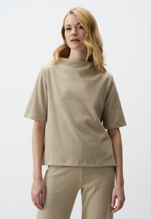 Top beige côtelé avec un col montant et des manches courtes. Texture douce, coupe décontractée, design minimaliste. Associé à un pantalon côtelé.