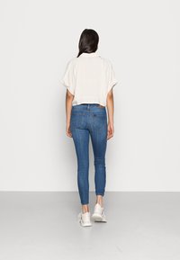 Kortärmad beige linne skjorta i cropped modell, kombinerad med blå skinny jeans. Vita sneakers; minimalistisk och avslappnad design.