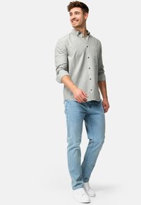 Camisa de botón de color gris claro con mangas largas, botones blancos, bolsillo en el pecho, combinada con jeans de color azul claro y zapatillas blancas.