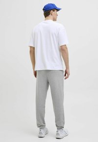 Hvid t-shirt med korte ærmer og grå sweatpants med elastiske manchetter, parret med en blå cap og hvide sporty sko. Simpelt design.