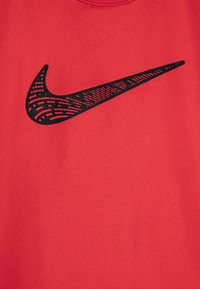 Röd tyg med en slät textur som har en stor svart Nike swoosh-logotyp, detaljerad med ett geometriskt mönster.