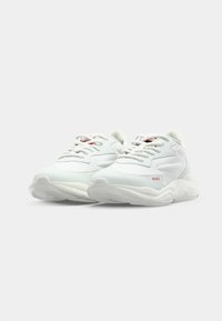 White sneakers with a smooth leather and textile upper, featuring a rounded toe, lacing system, and subtle red branding on the side.