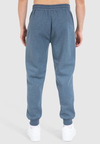 Blauwe katoenen sweatpants met een elastische tailleband en cuffed enkels, gekenmerkt door een zachte textuur en een relaxte pasvorm. Gecombineerd met witte sneakers.