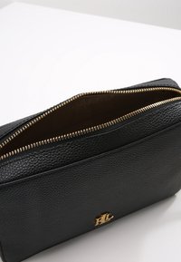 Černá texturovaná kožená peněženka se zlatým zipem, s otevřeným vrchem a výrazným zlatým logem na přední straně.