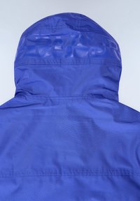Modrá dešťová bunda s hladkým, lesklým povrchem, vybavená kapucí a logem vytištěným na horní straně. Navržena pro voděodolnou ochranu.