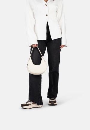 Blazer blanc cintré avec des boutons dorés, porté sur un jean noir et des baskets claires, tenant un petit sac hobo blanc de forme courbe.