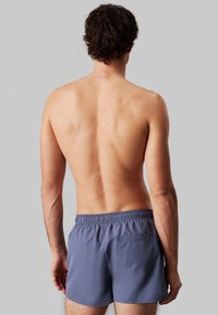 Bermuda da nuoto da uomo in tessuto blu tenue con cintura elastica, dotato di tasca posteriore e una texture liscia e leggera.
