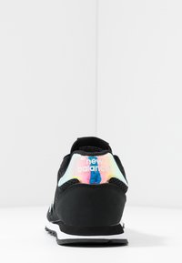 Svart sneaker med mesh- och syntetiskt överdrag, med en reflekterande, flerfärgad hälla och vit sula. Logotyp synlig på hälen.