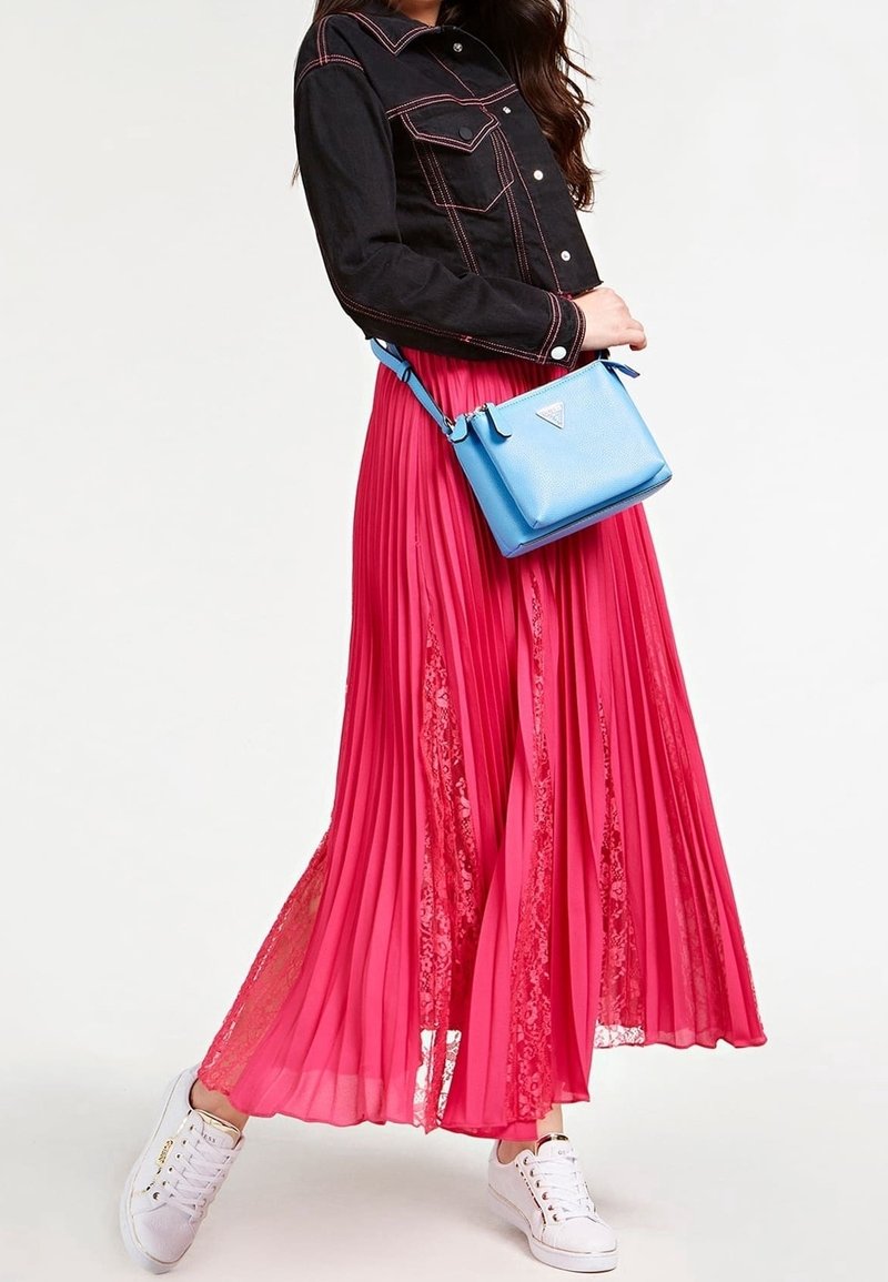Giacca in denim nera con gonna pieghettata rosa e sneakers bianche. Una borsa a tracolla blu aggiunge un tocco di colore. La gonna presenta dettagli in pizzo.