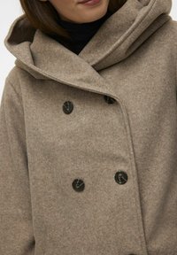 Cappotto doppiopetto marrone in morbida lana, con cappuccio grande, bottoni neri e una texture liscia.