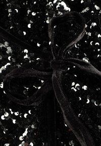 Tissu noir à sequins avec un ruban doux en velours. Les sequins sont circulaires et réfléchissants, créant une texture scintillante sur toute la matière.