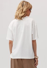 Biała, oversize koszulka t-shirt z bawełny, z okrągłym dekoltem, krótkimi rękawami i luźnym krojem o gładkiej fakturze. Przedstawiono widok z tyłu.