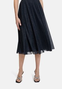 Jupe A-line bleu marine avec une texture scintillante, assortie à des sandales noires à lanières ornées de strass et à bout carré.