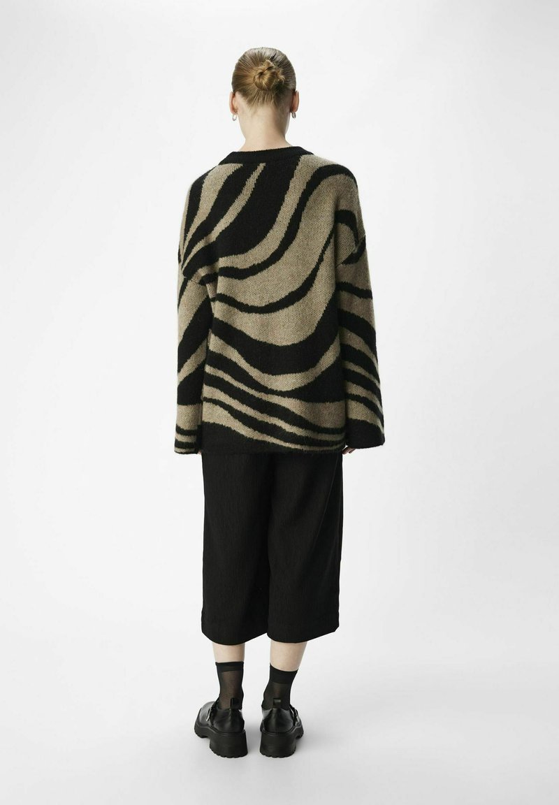 Übergroßer schwarzer und khakifarbener Pullover mit welligen Streifen, kombiniert mit schwarzen Culottes und klobigen schwarzen Schuhen. Glatte Textur, lässiges Design.