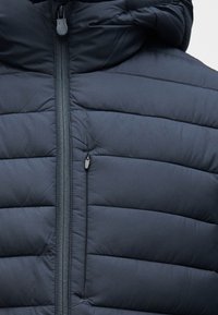 Μπουφάν navy blue με οριζόντιο καπιτονέ σχέδιο, πλήρης φερμουάρ μπροστά και κουκούλα. Διαθέτει υφασμάτινη υφή και μικρό τσεπάκι με φερμουάρ.