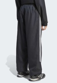 Crne sportske hlače s elastičnim pojasom, s bijelim vertikalnim prugama sa svake strane. Uparene s crnim tenisicama.