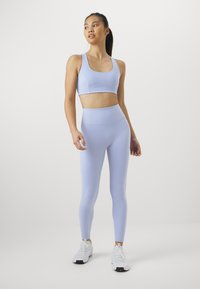 Világos lila sportmelltartó és magas derekú leggings sima anyagból. Fehér sportcipők fekete részletekkel. Egyszerű, testhezálló dizájn.
